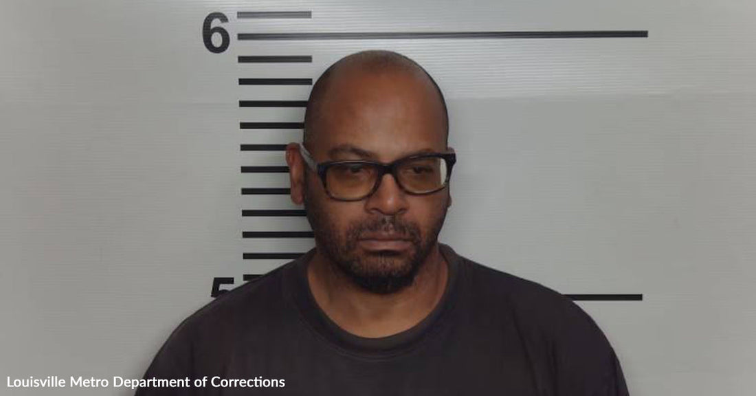 Mugshot of a man wearing glasses in front of a height chart, facing forward with a neutral expression.