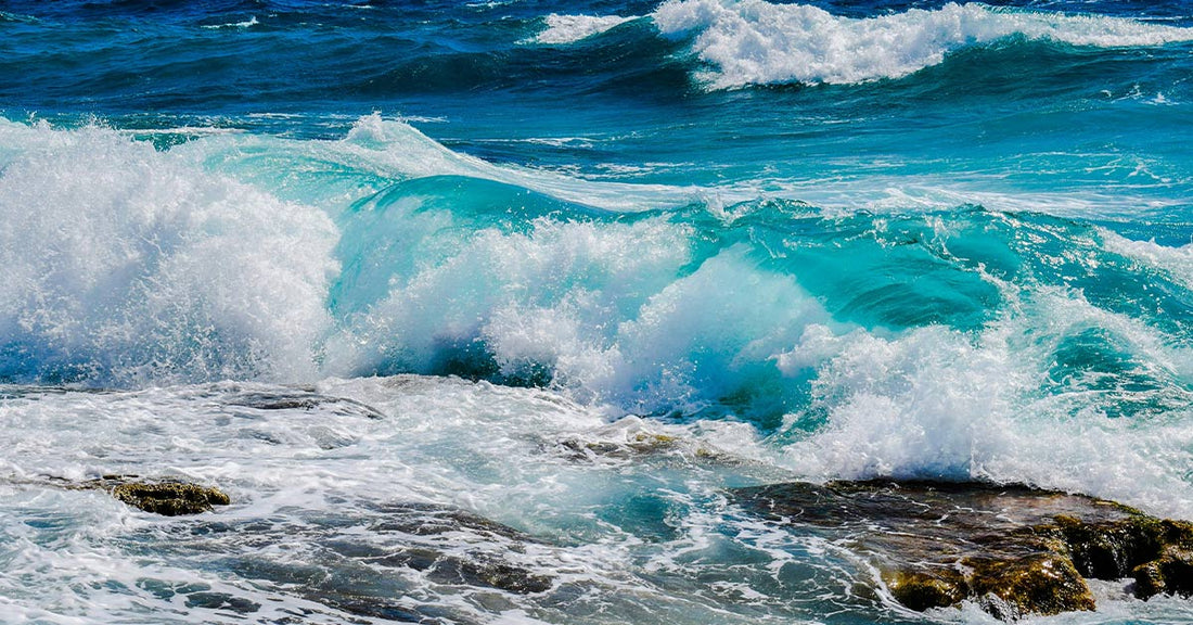 Turquoise waves crash against rocks, creating frothy white spray in sunlight.
