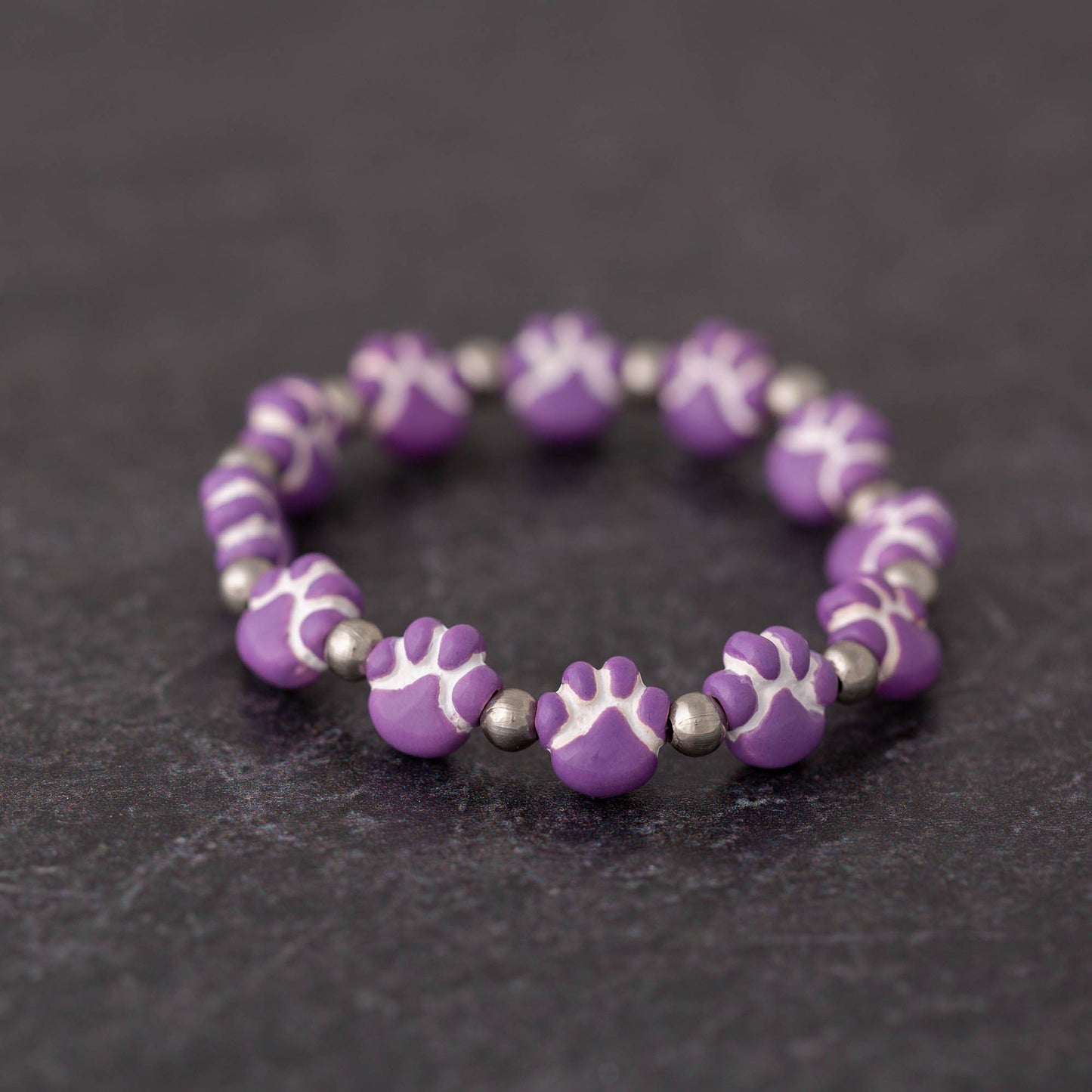 ceramic purple paw print beads on a bracelet with a black background