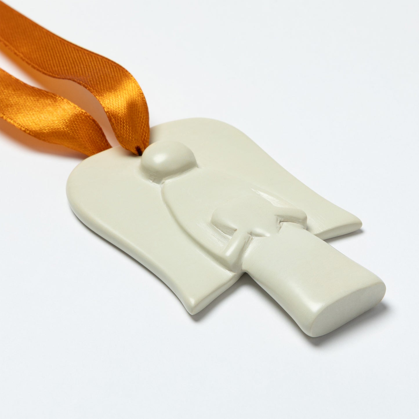 White soapstone ornament shaped like a an angel holding a heart, with an orange ribbon on a white background