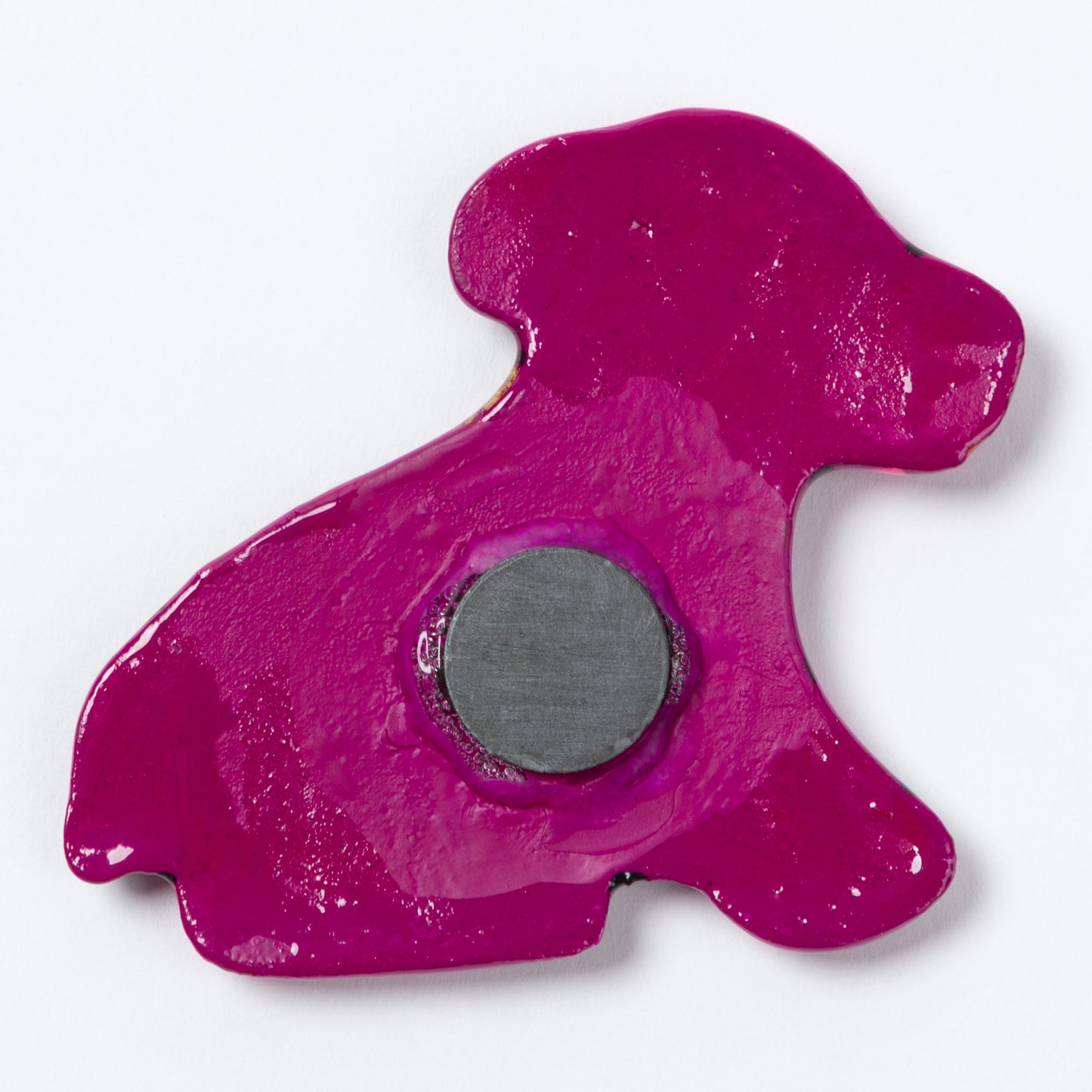 The back of a fuchsia dog-shaped magnet with a circular gray magnet in the center, shown on a plain white background.