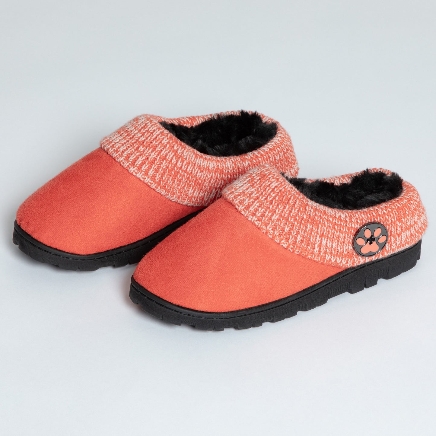 Coral clog slippers with coral knitted cuffs, a paw print button on the side, with sturdy black outsoles, on a white background.