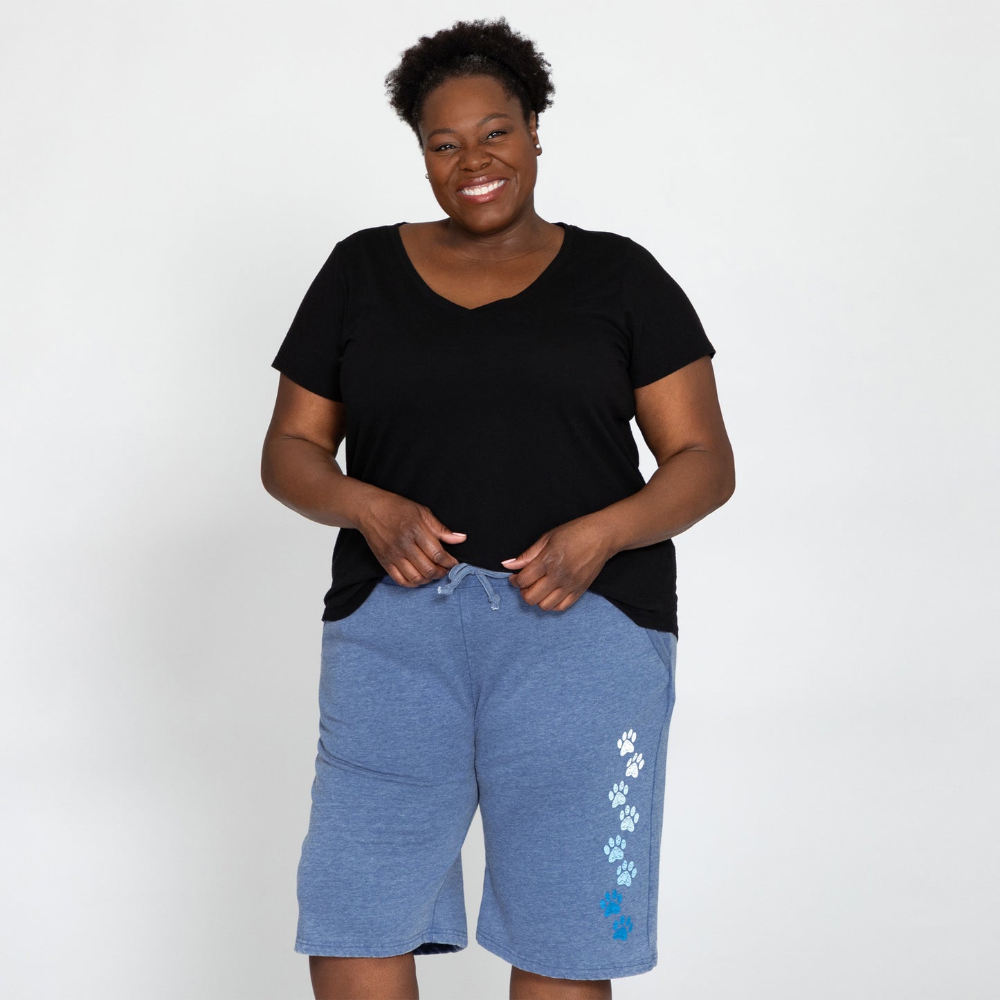 A woman wearing a pair of blue burnout board shorts with a pattern of white paw prints on the left leg, featuring an elastic drawstring waistband and two side pockets.