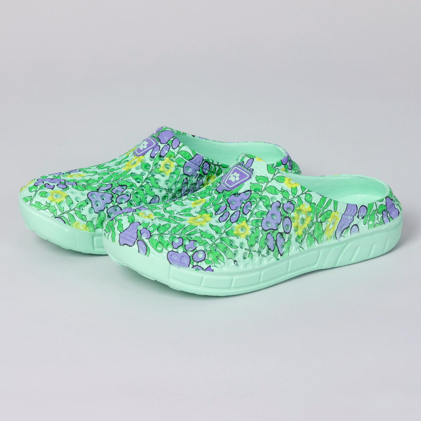 Light green clogs featuring a vibrant floral and paw print pattern in shades of purple and yellow.