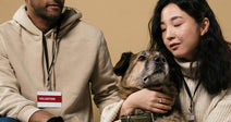 Two volunteers gently interact with a dog against a neutral background.