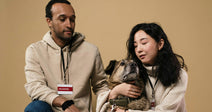 Two volunteers sitting with a dog against a neutral backdrop.