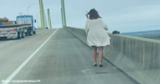 Person in a white outfit stands on a bridge, wind blowing against them.