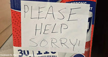 A handwritten sign taped to a package reads “PLEASE HELP SORRY!” in large block letters.