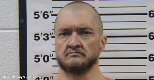 Mugshot-style photo of a bald man in front of a height chart.