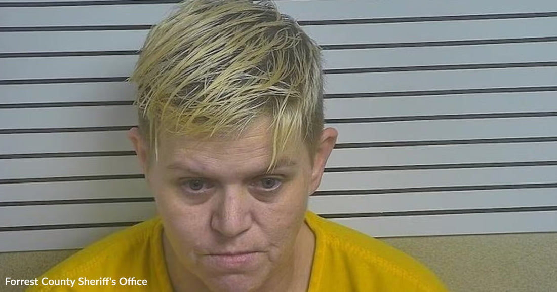 Mugshot of a woman with short blond hair wearing a yellow shirt in front of booking height lines.