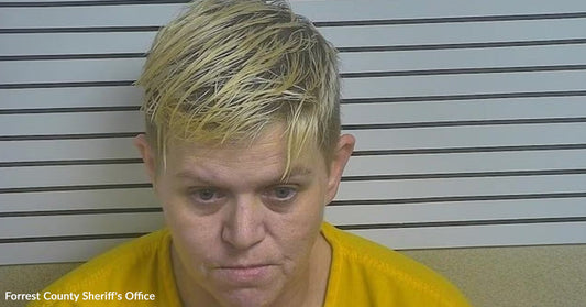 Mugshot of a woman with short blond hair wearing a yellow shirt in front of booking height lines.