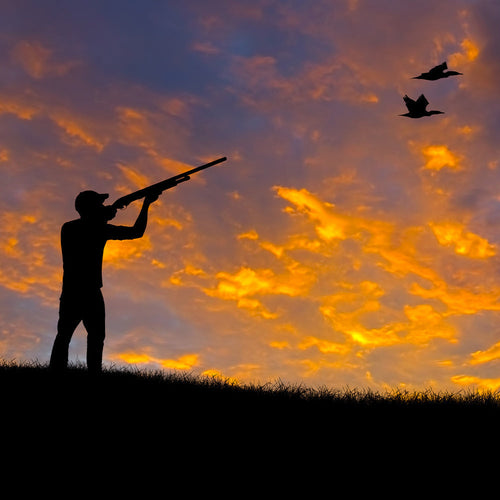 Silhouette of a hunter aiming a shotgun on a ridge at sunset, with glowing orange clouds filling the sky.