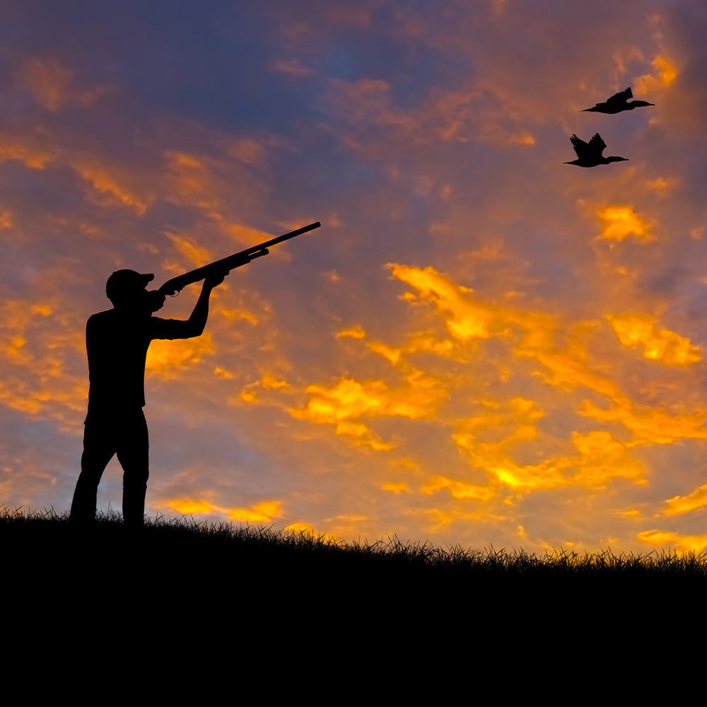 Silhouette of a hunter aiming a shotgun on a ridge at sunset, with glowing orange clouds filling the sky.