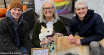 Two young men and an older woman smiling with a newly adopted dog while holding a “Found My Furever @ Tails Rescue” sign outdoors.