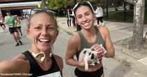 Two smiling runners take a selfie during a marathon while one of them gently holds a small black-and-white kitten.