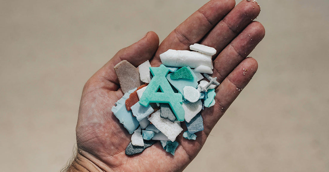 A hand holding a collection of small plastic fragments and debris, including an aqua-colored letter “A.”
