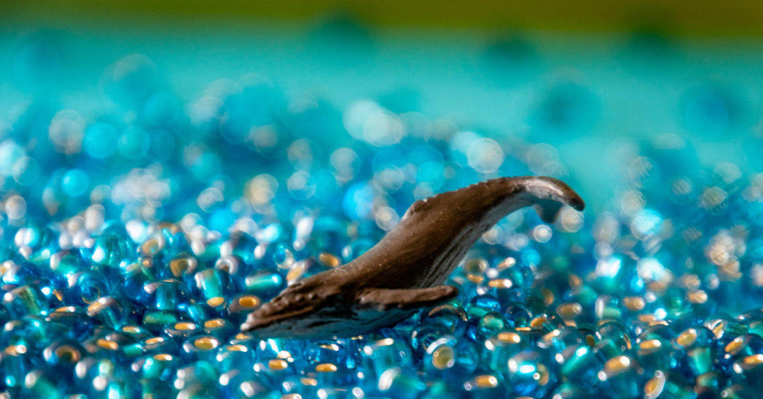 A small, dark figure resembling a fish swims among shimmering blue beads.