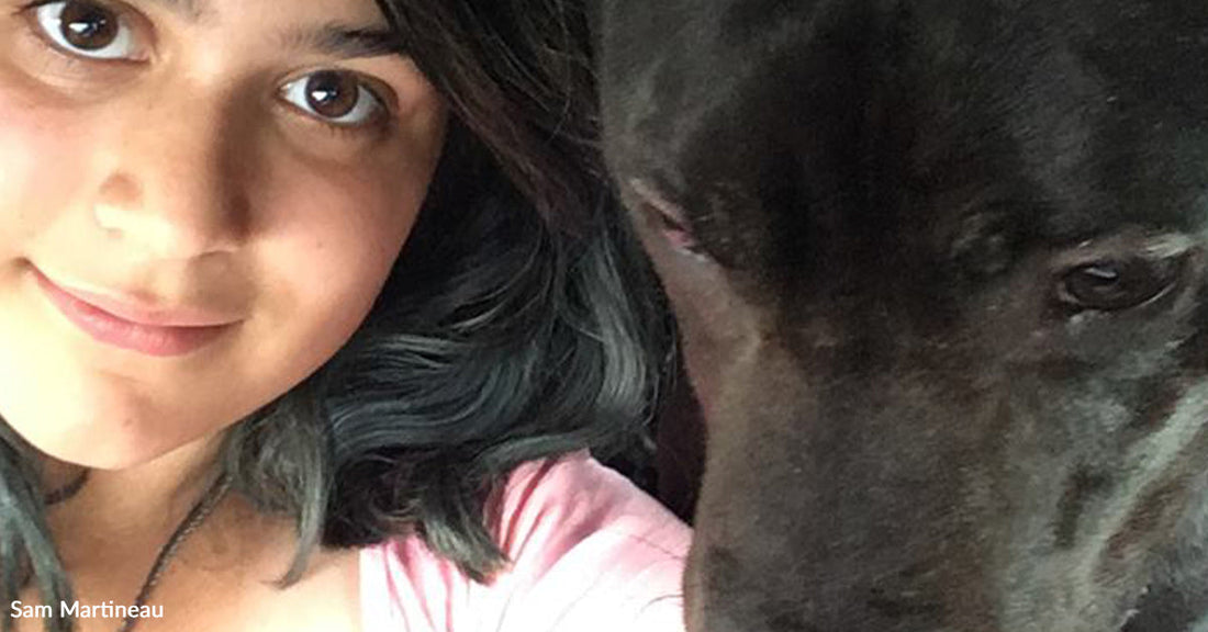 Young woman taking a selfie inside a car with a large black dog resting its head beside her.