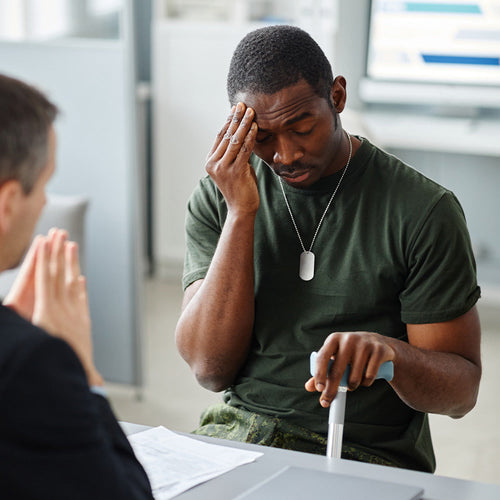 Veteran with a cane looks distressed during an office meeting, touching his forehead while speaking with an official.
