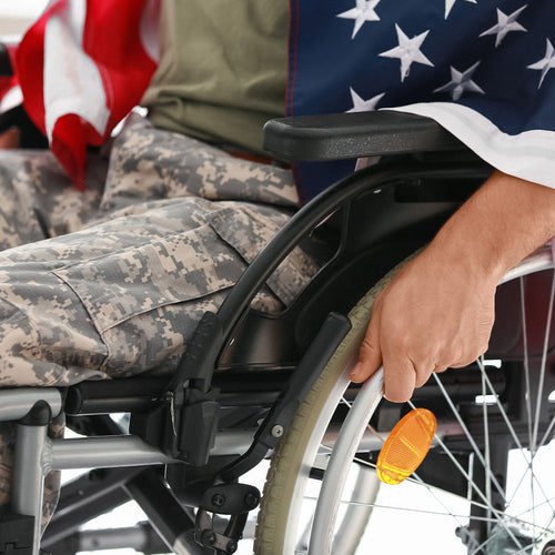 Close-up of a veteran seated in a wheelchair, one hand on the wheel, with an American flag draped across their lap.