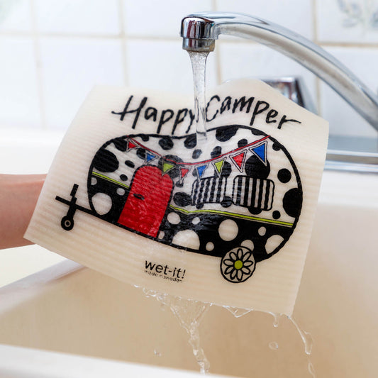 Hand holding a 'Happy Camper' towel over a sink with a faucet pouring water over it.