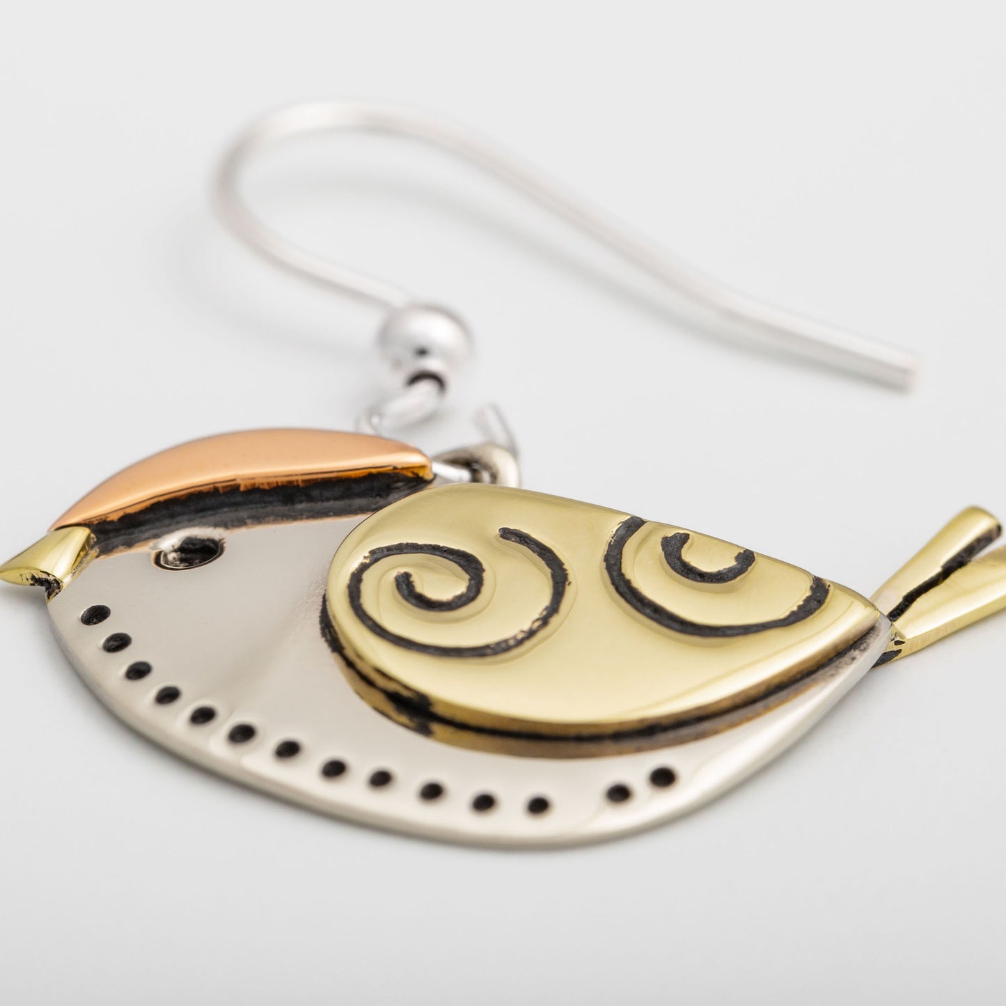 Brass and silver bird shaped earring with spiral design on a white background.