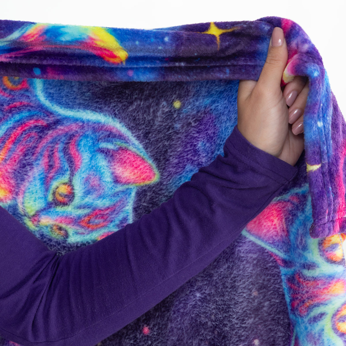 A close-up of a person holding up a plush blanket featuring a colorful cosmic cat design with a purple long-sleeve shirt visible.