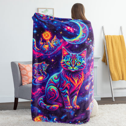A person stands with their back to the camera wrapped in a colorful blanket featuring a psychedelic cosmic cat design. The blanket displays a large, vibrant neon cat in the center surrounded by stars, a crescent moon, and swirling galaxy patterns in purple, blue, pink, and orange.
