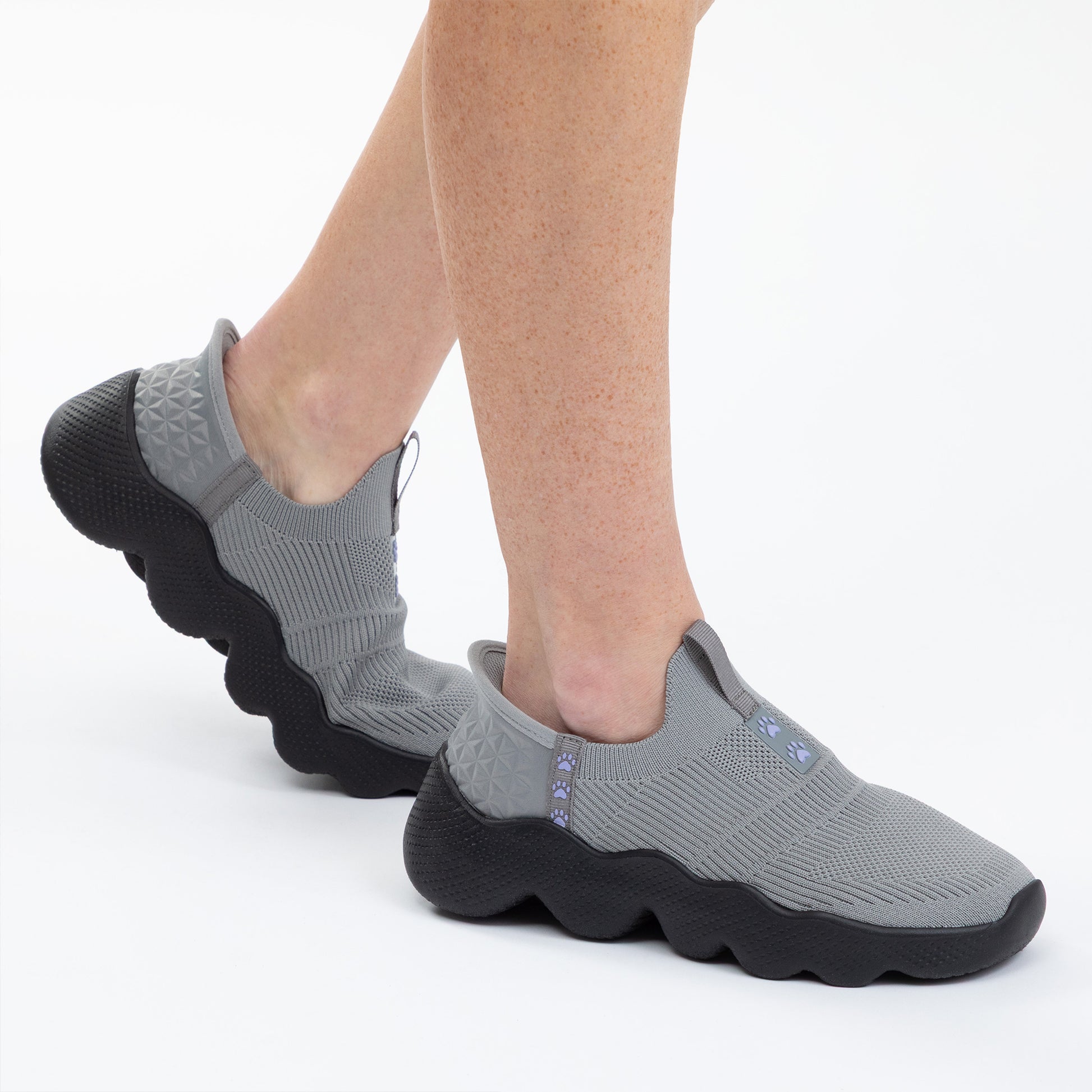 Gray slip-on shoes with black soles worn by a person on a white background