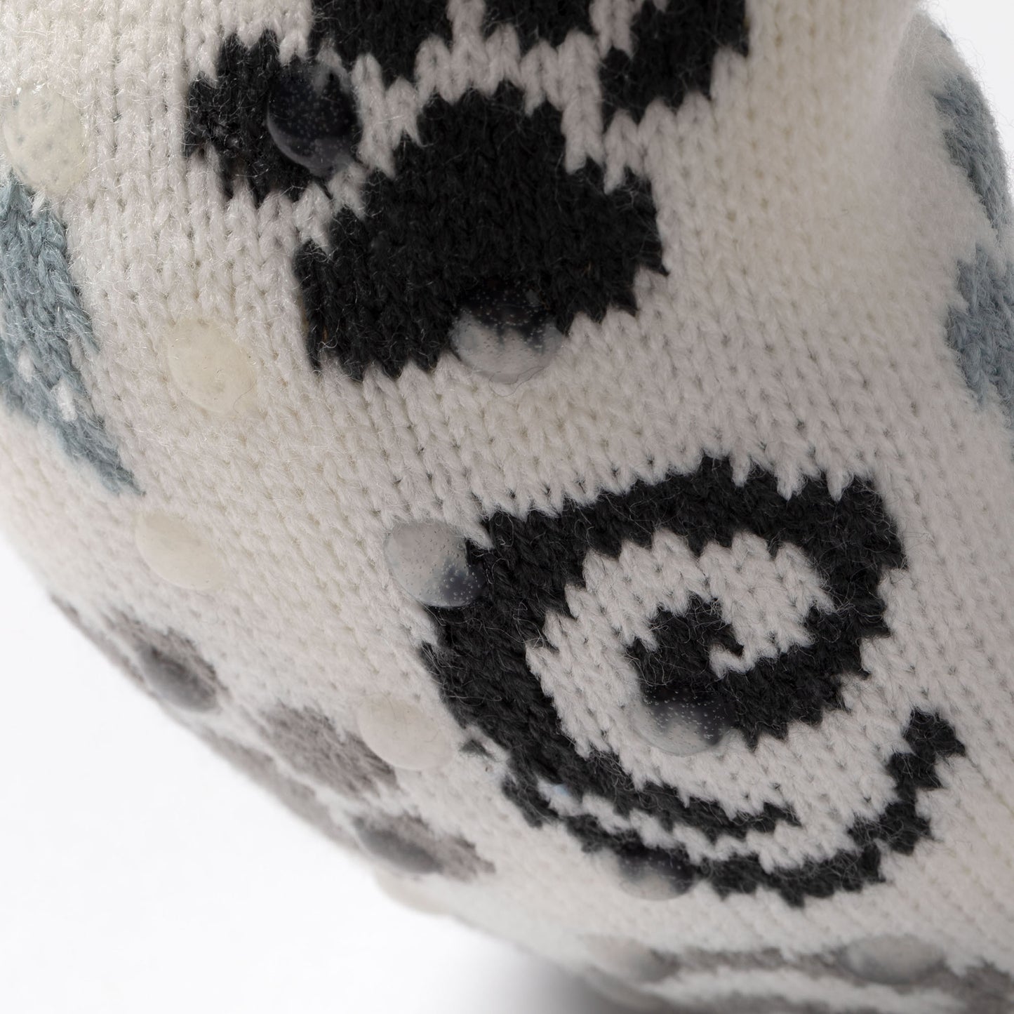 close up of white, blue, gray paw patterned knitted slipper socks, on a carpet floor blue gray paws swirls, showing traction dots