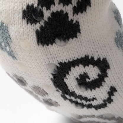 close up of white, blue, gray paw patterned knitted slipper socks, on a carpet floor blue gray paws swirls, showing traction dots