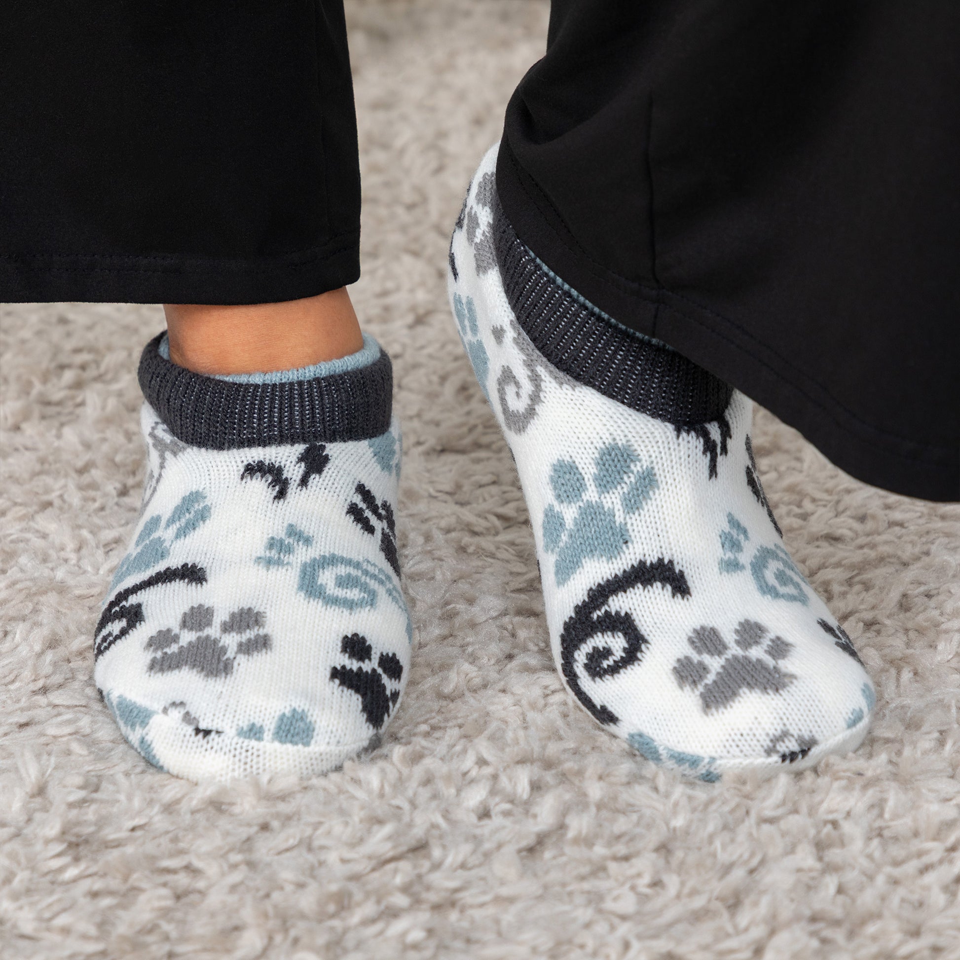 Person wearing white, blue, gray paw patterned knitted slipper socks, on a carpet floor blue gray paws swirls