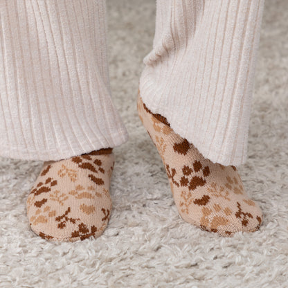 Person wearing brown and beige paw patterned knitted slipper socks, on a carpet floor brown paw sprig