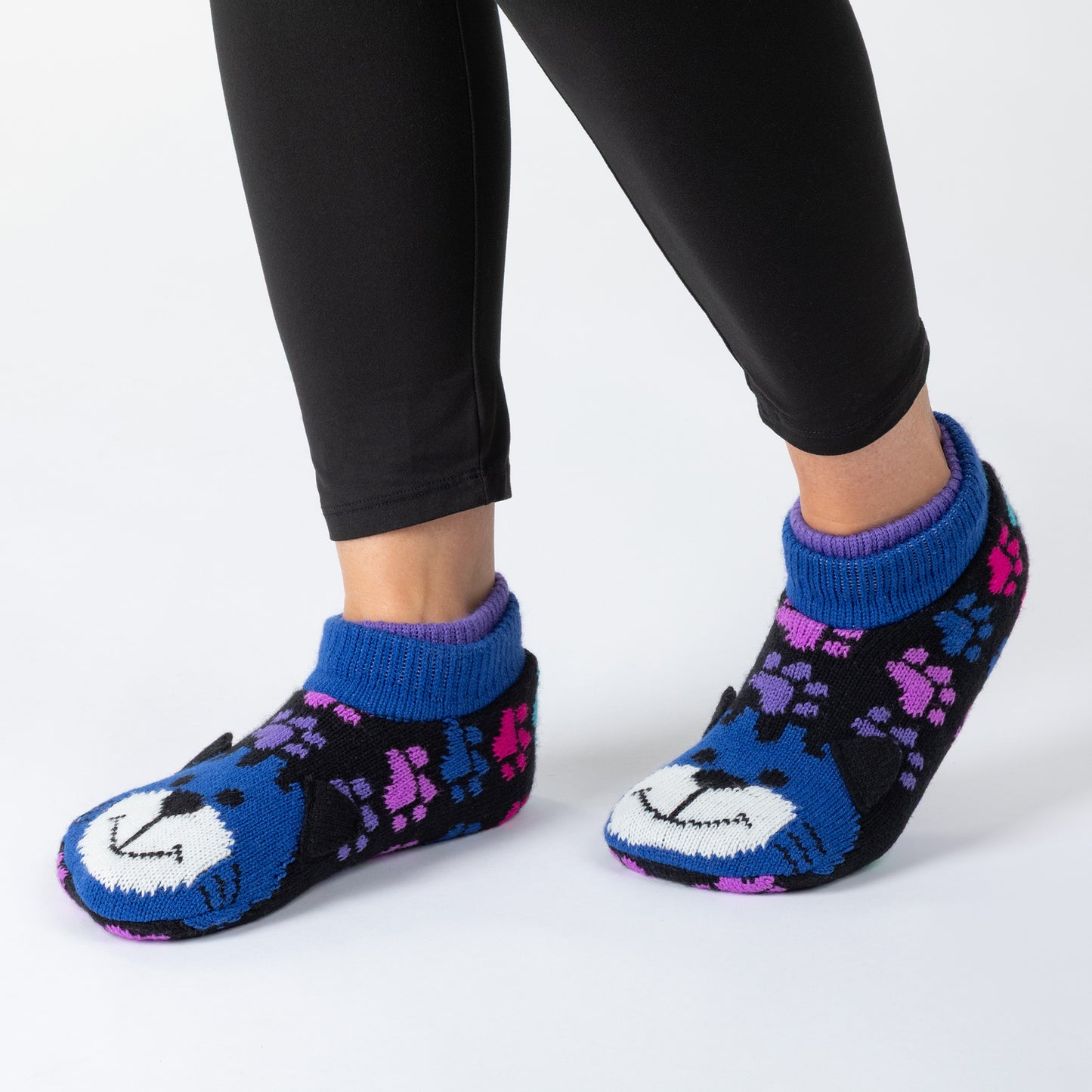 A person wearing black leggings and blue knit booties with a cat face design and purple pattern details, against a white background.