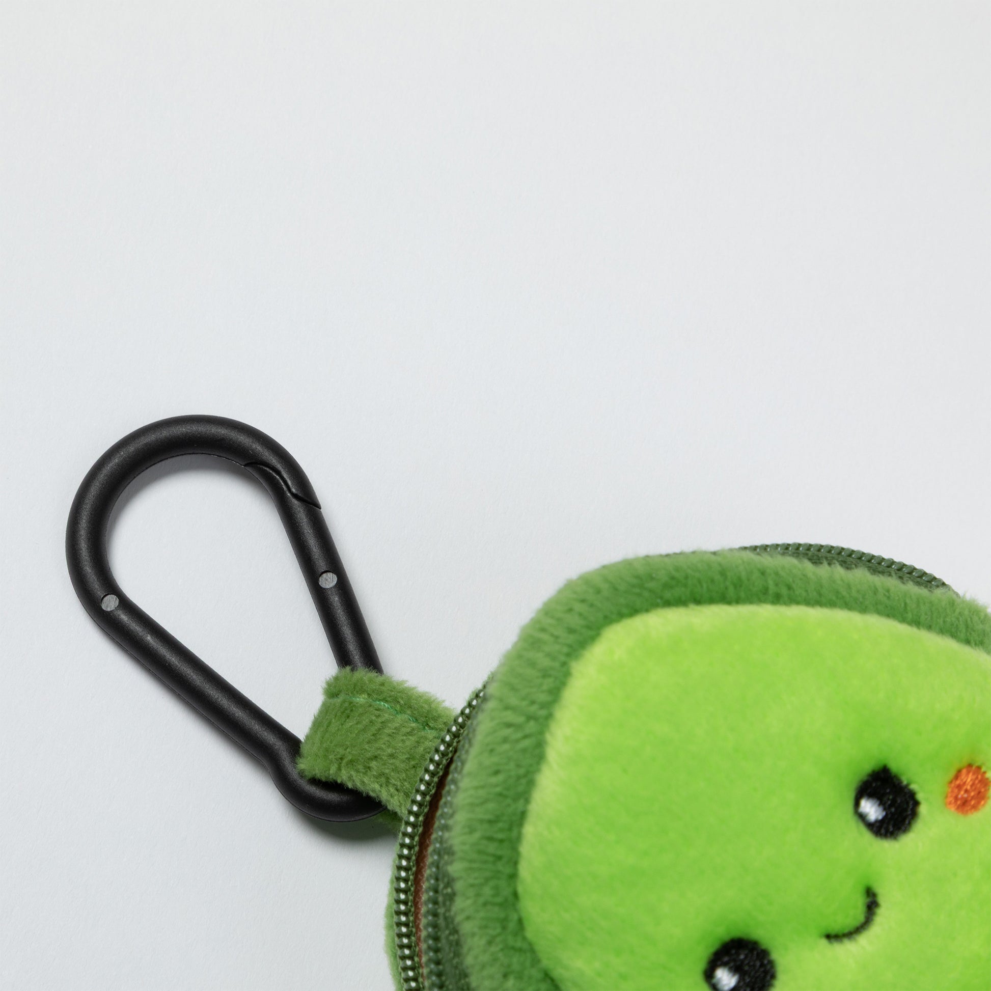 Green plush avocado-shaped keychain with a carabiner for pet waste bags on a light gray background.