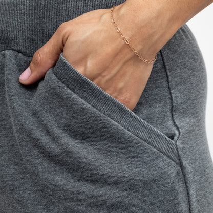Person wearing a gray pair of shorts with a gold bracelet on a plain background