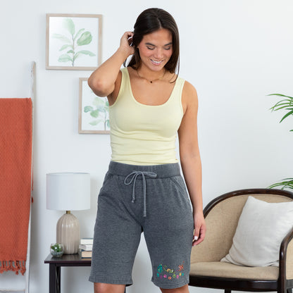 Woman wearing a yellow tank top and gray shorts with cats on them, in a living room setting.