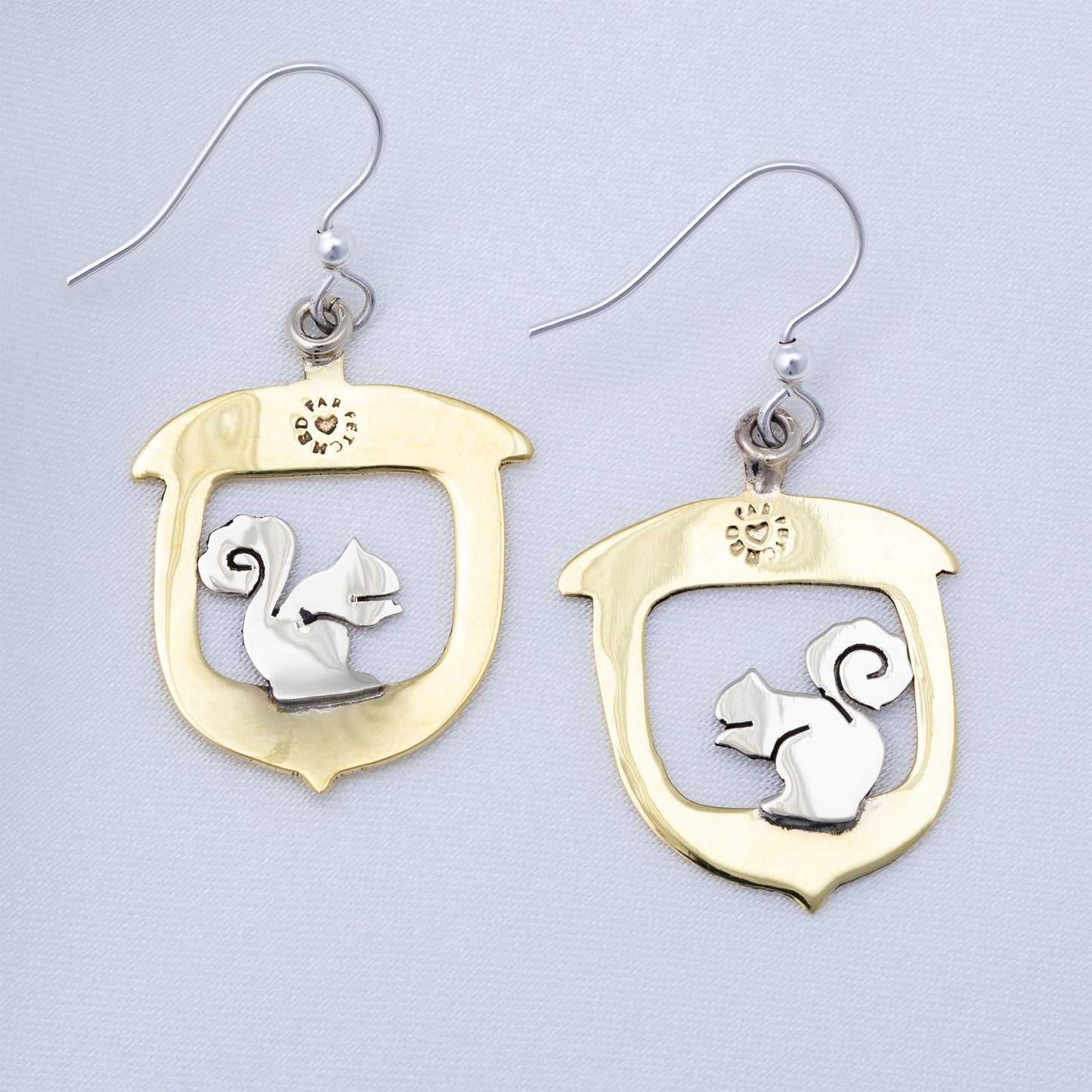 Brass and silver earring backings with squirrel design on a light gray background