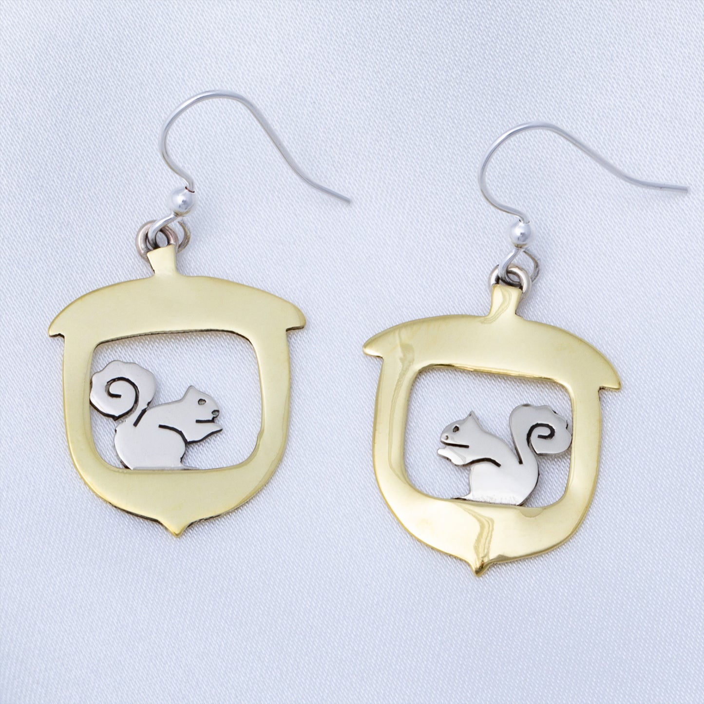 Brass and silver earrings with a squirrel design on a light gray background.