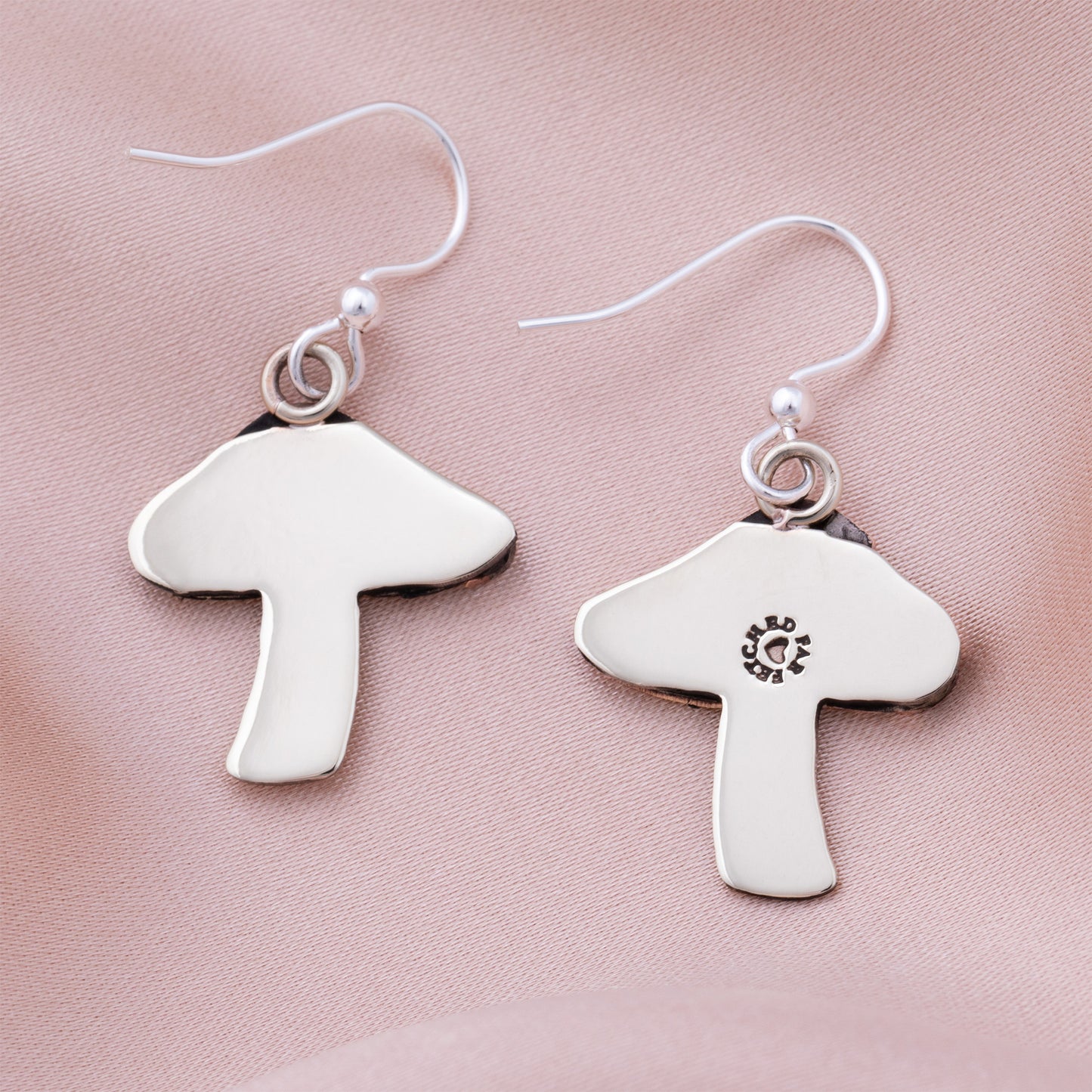Silver mushroom-shaped earring backs on a pink satin background.