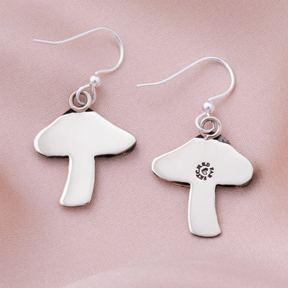 Silver mushroom-shaped earring backs on a pink satin background.