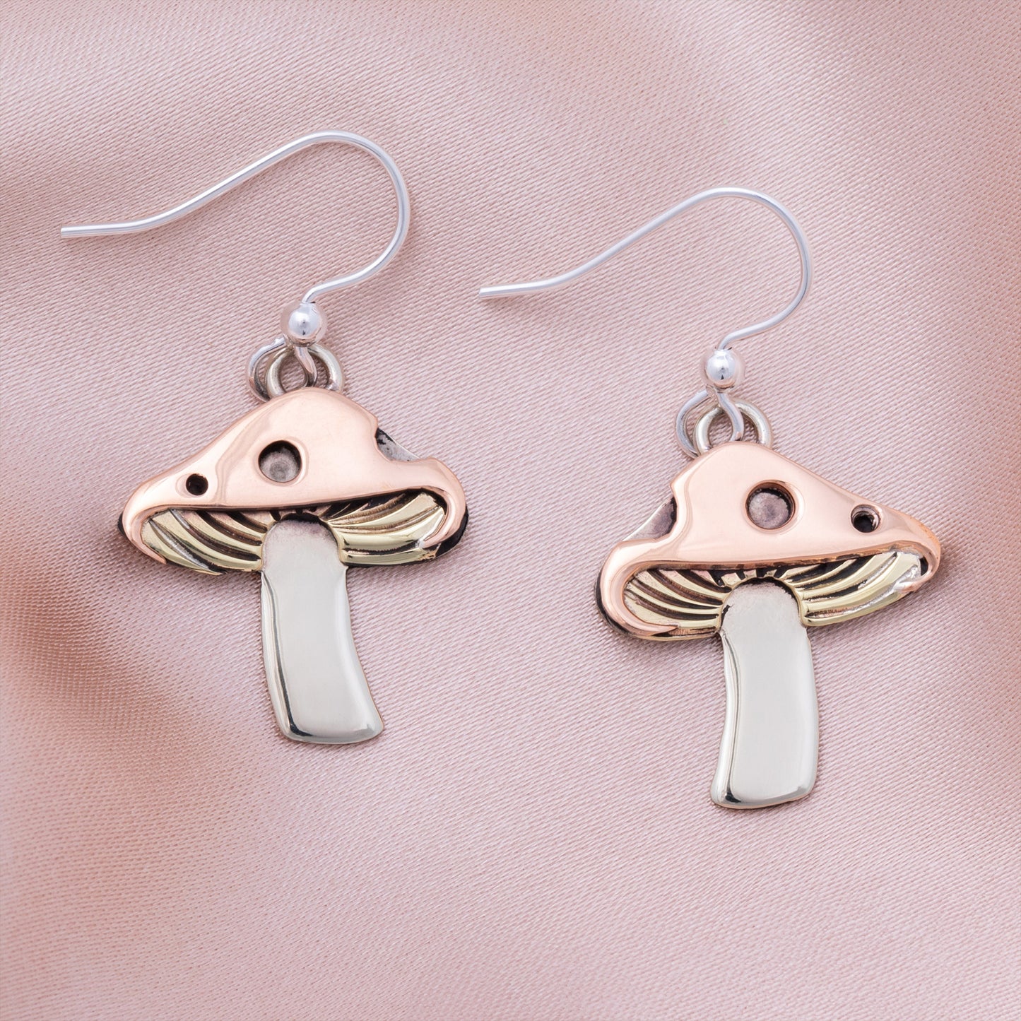 Mushroom-shaped earrings with copper, brass, and silver, on a pink satin background.