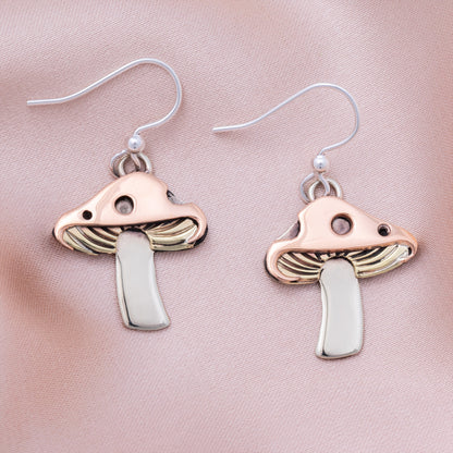 Mushroom-shaped earrings with copper, brass, and silver, on a pink satin background.