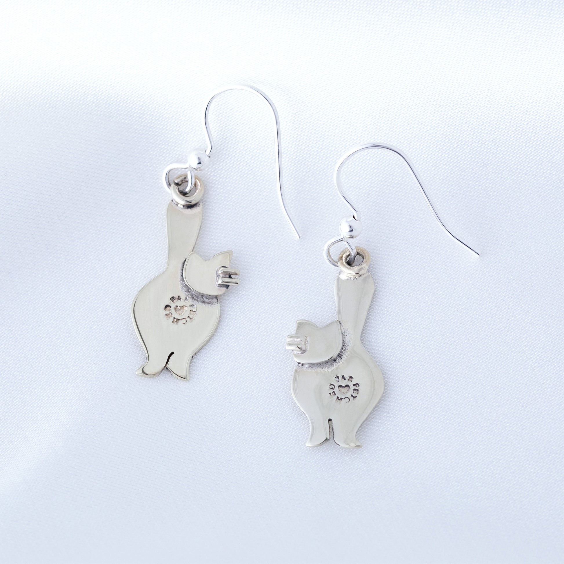 The back of silver cat-shaped earrings on a light gray background