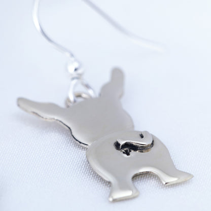 Silver earring pendant of a dog's behind on a white background