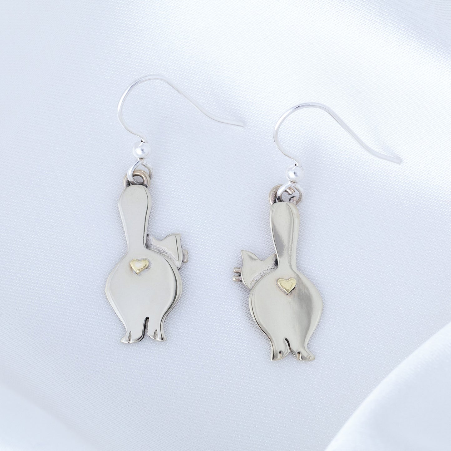 Silver cat-shaped earrings with heart details on a light gray background