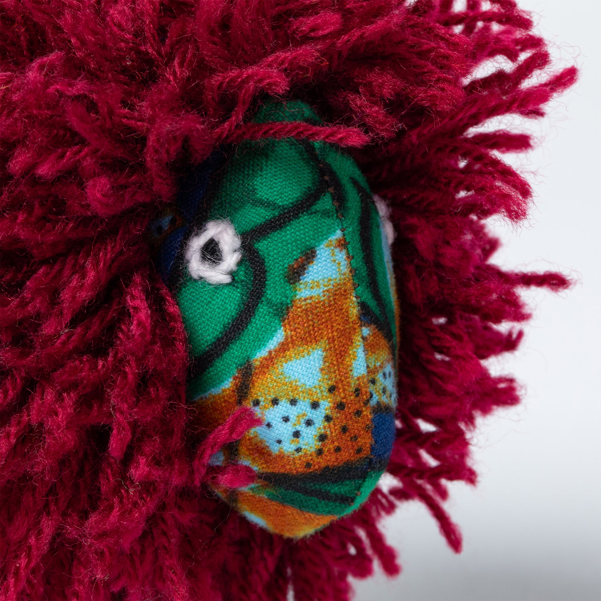 Close up of a lion ornament made of colorful fabric and a red yarn mane