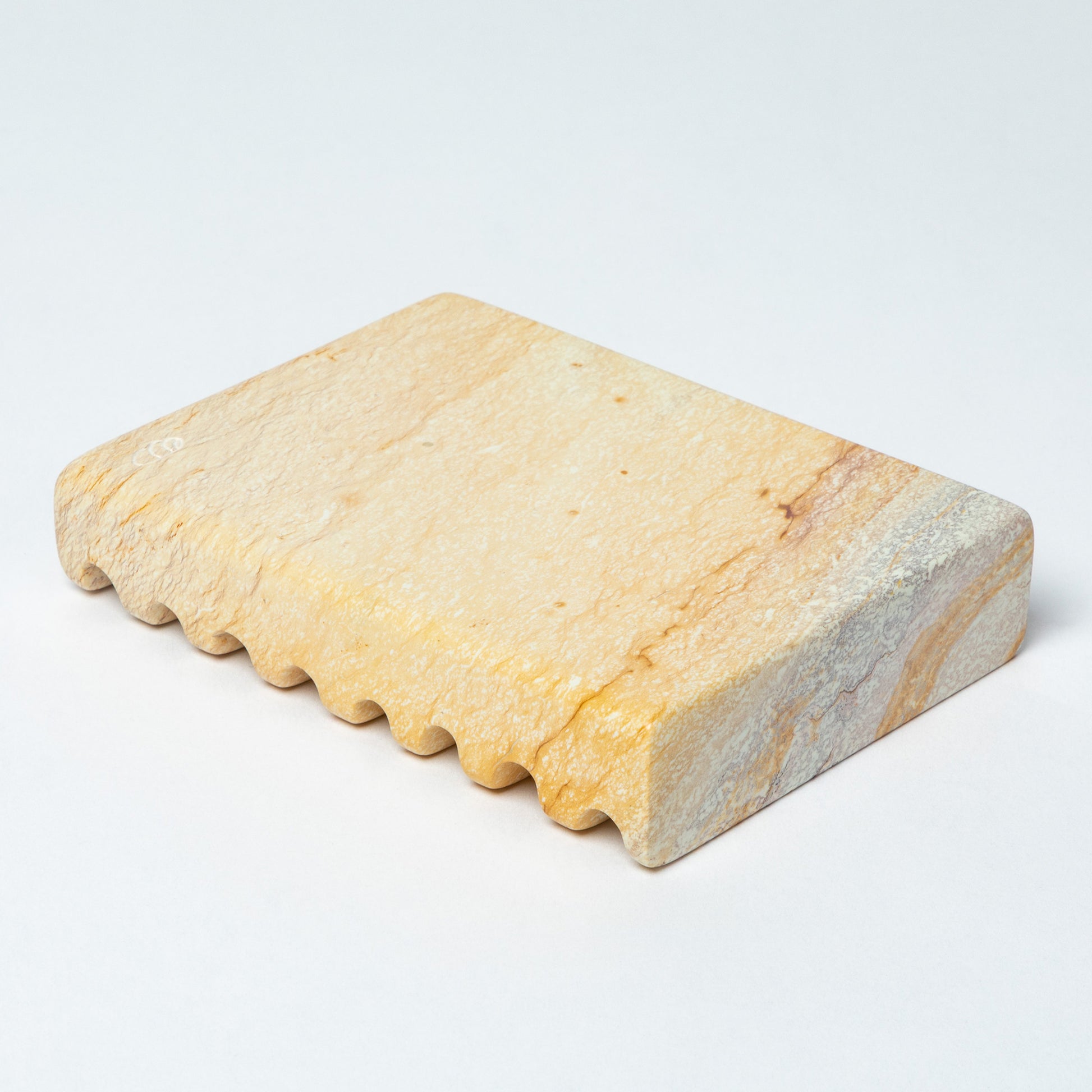 The bottom of a yellow soapstone soap dish, against a white background.