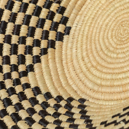Close-up of a hand woven raffia bowl with black and beige pattern