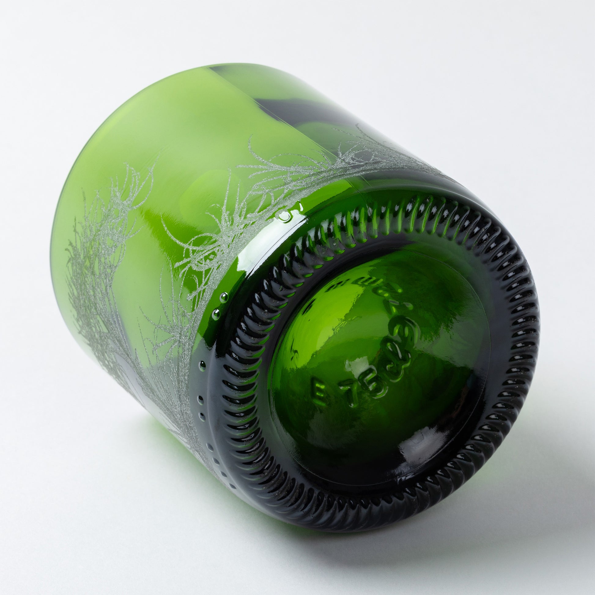 Green glass bottle with decorative etching on a white background